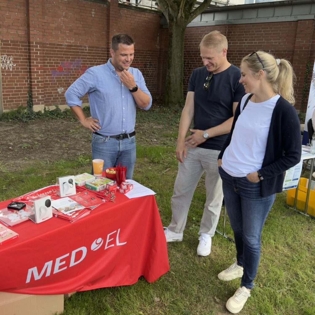 Florian Krieger von MED-EL (links) mit der Familie Strieth am Informationsstand des Unternehmens.